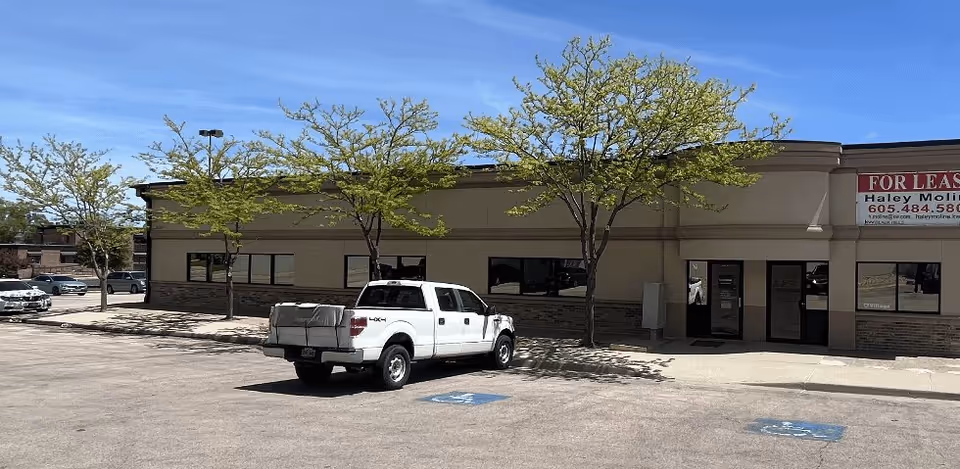 Exterior view of a beige commercial building with a parking lot and a white pickup truck.