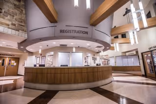 Registration desk in a spacious lobby with a curved wood counter and hanging light fixtures.