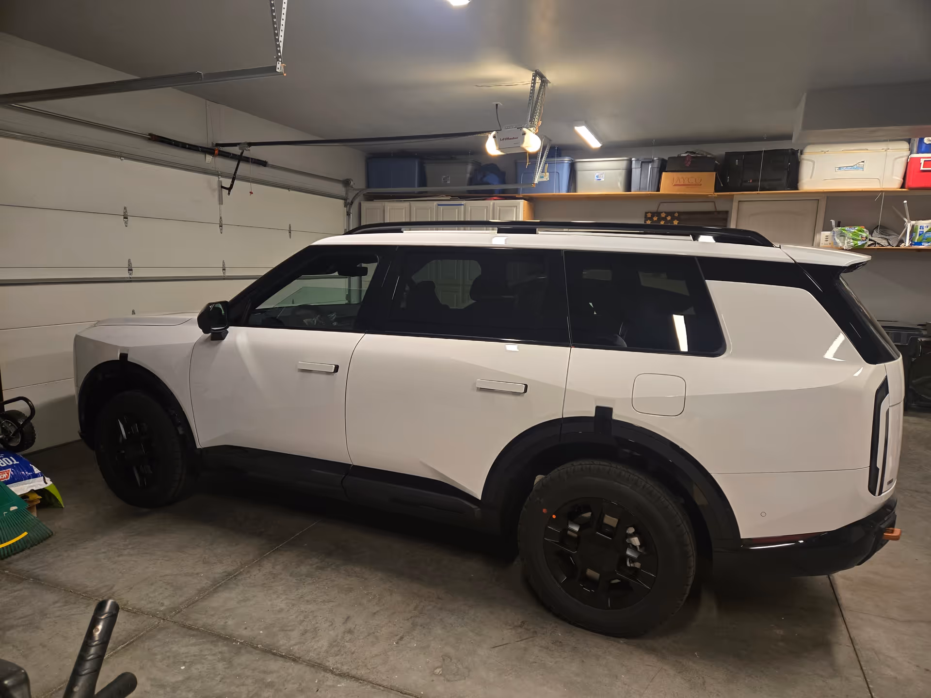 White SUV parked inside a cluttered garage with shelves and boxes overhead.