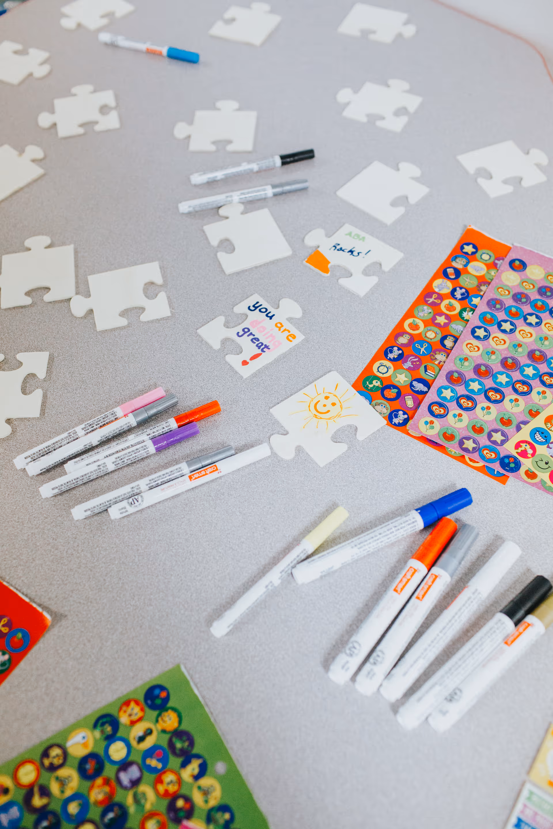 Craft activity table with puzzle pieces, markers, and colorful stickers in a bright interior room.