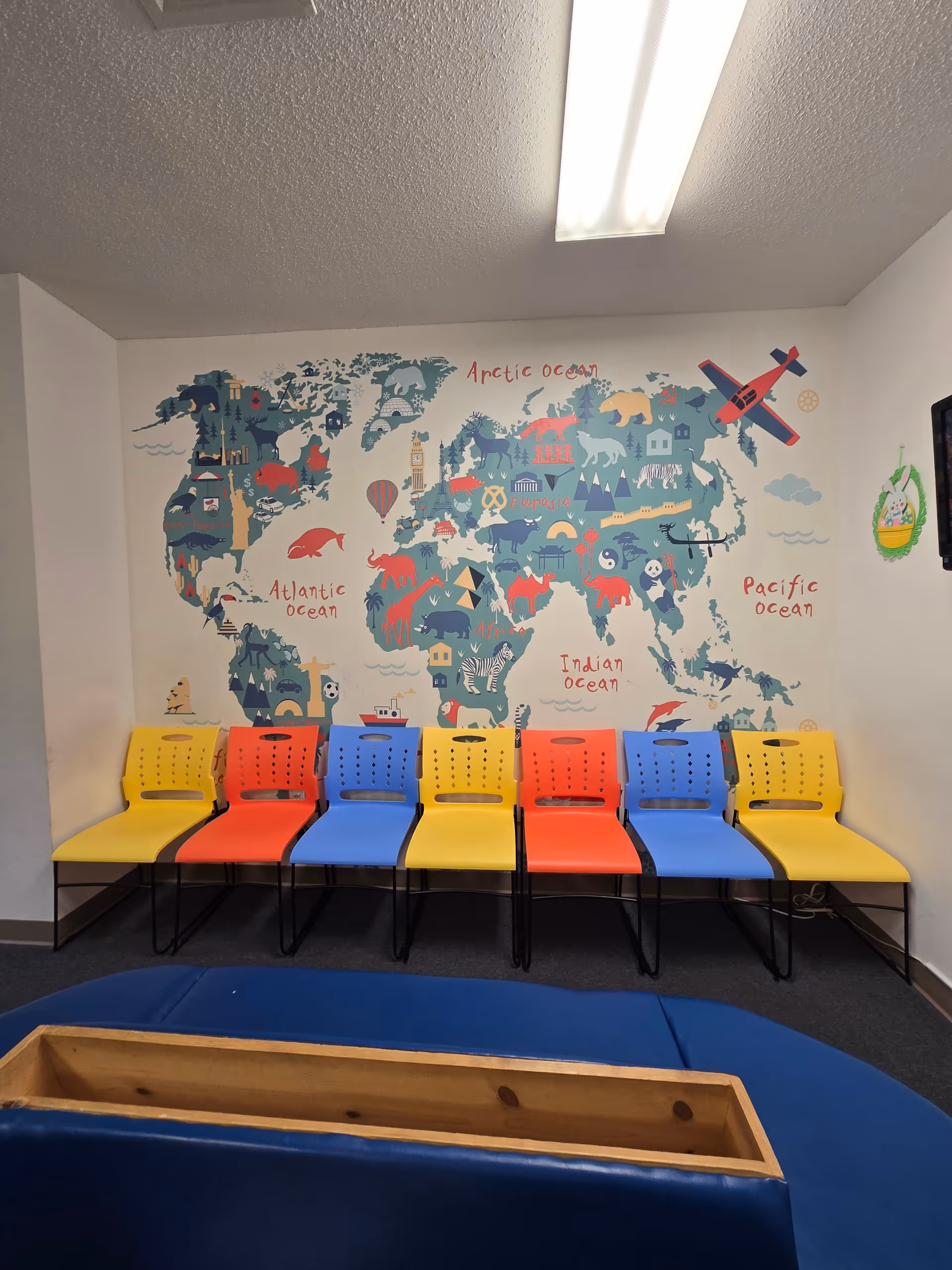 Row of colorful plastic chairs along a wall with a world map mural.