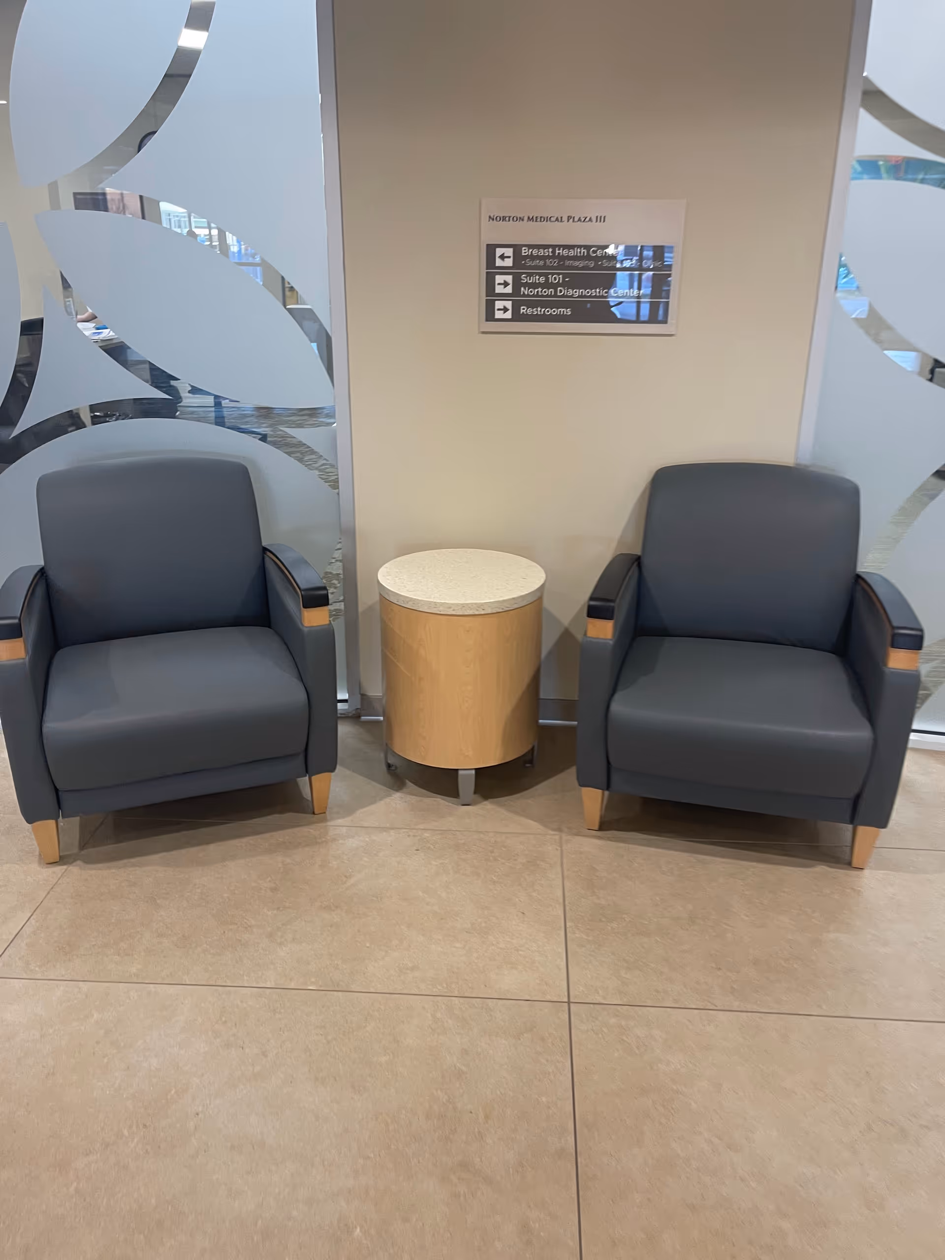 Two blue-gray armchairs flank a small round table in a modern medical plaza lobby.
