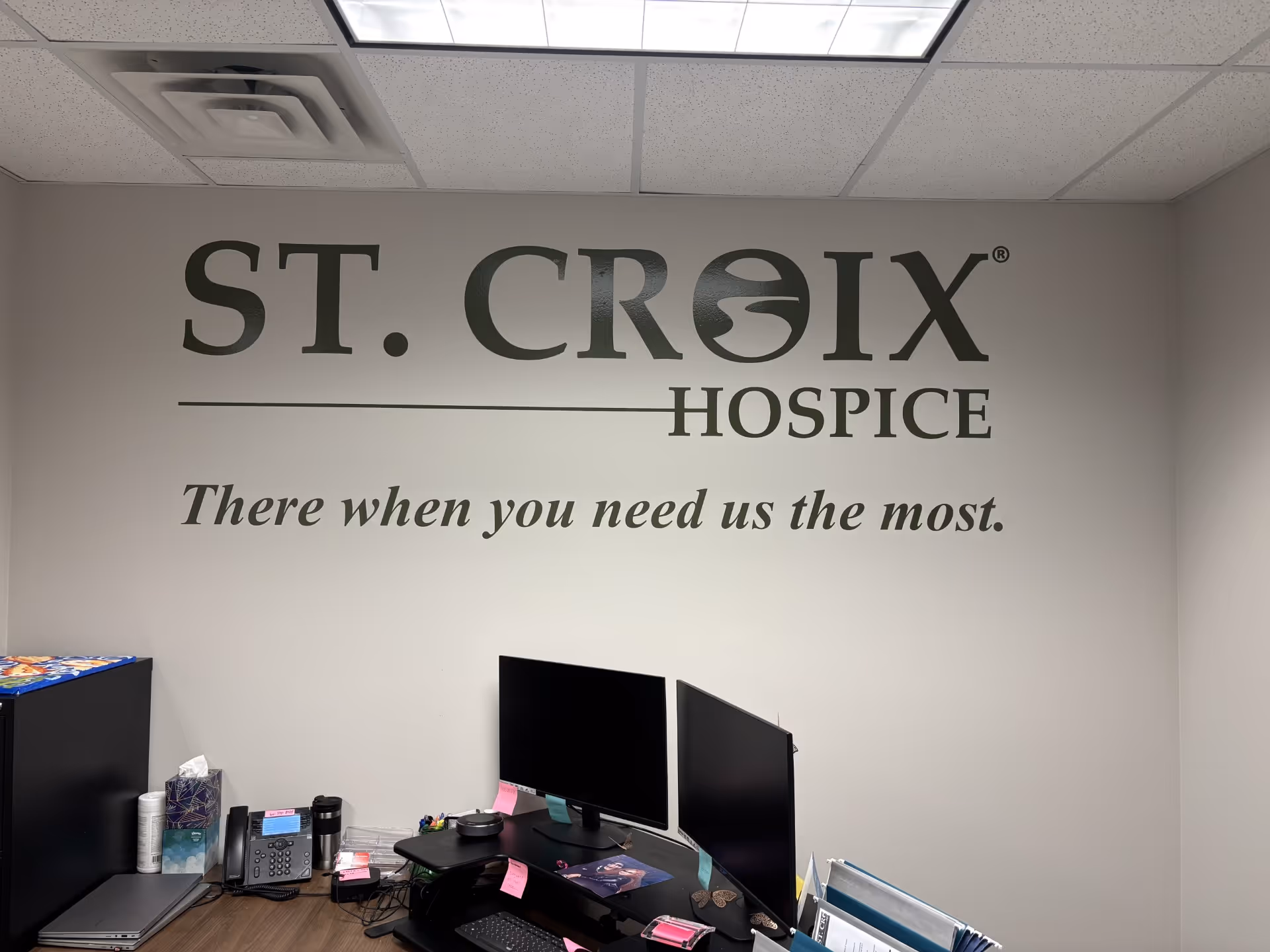 Office workspace with St. Croix Hospice logo on the wall behind a computer desk.