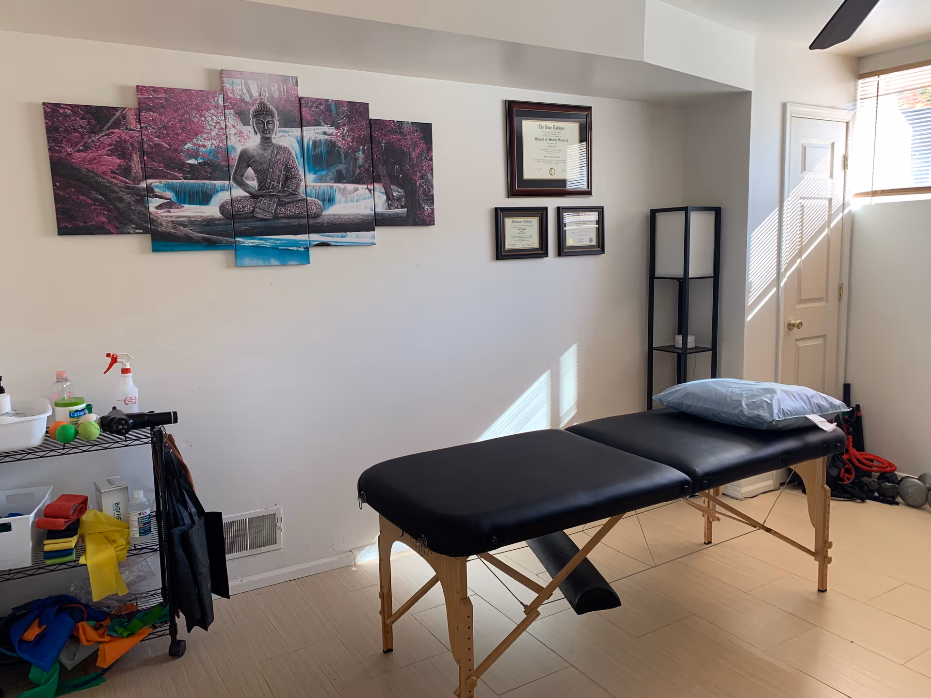 A massage therapy table in a clean room with wall art and diplomas