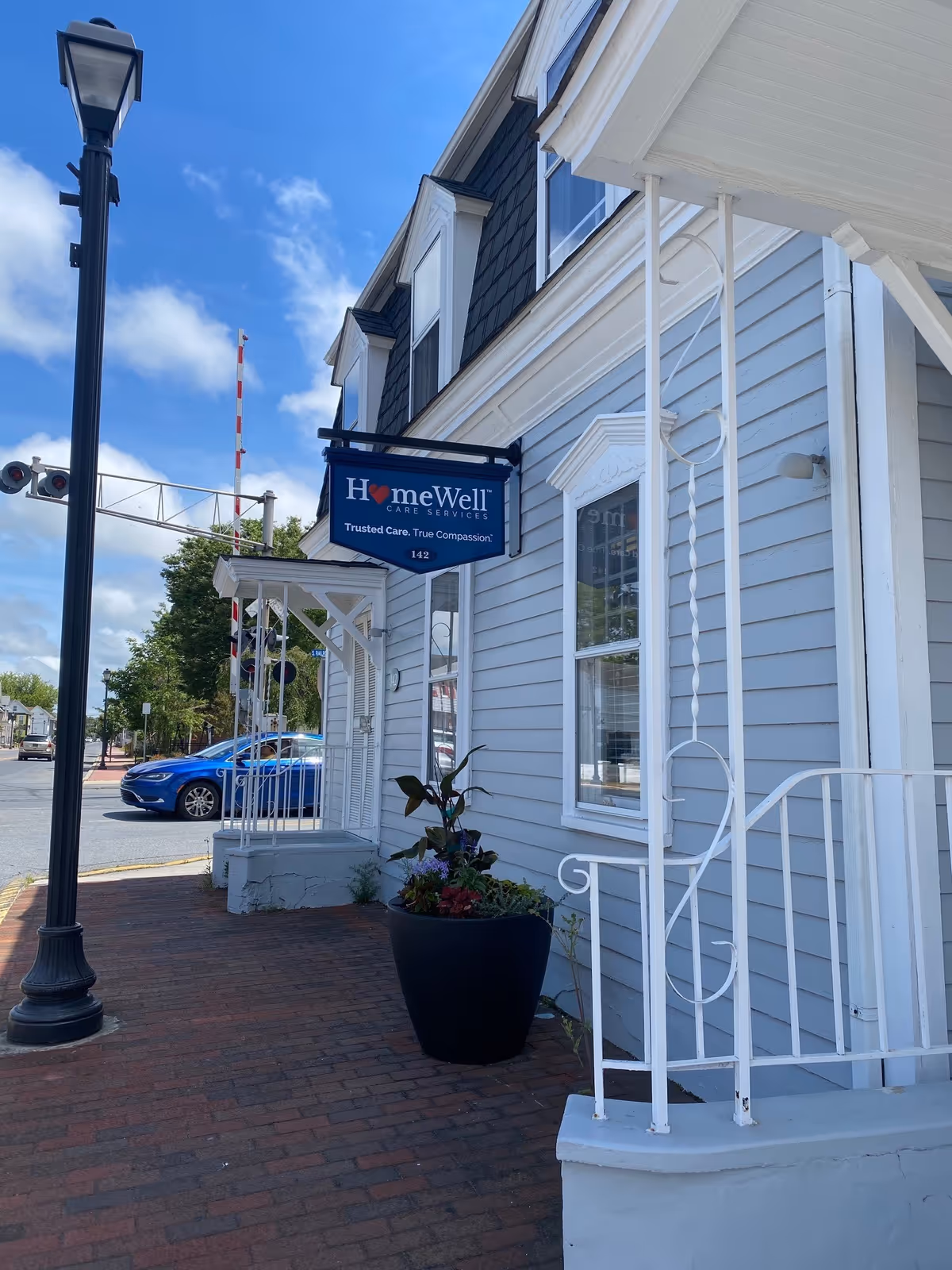 Exterior view of a HomeWell Care Services building with a blue sign along a brick sidewalk.