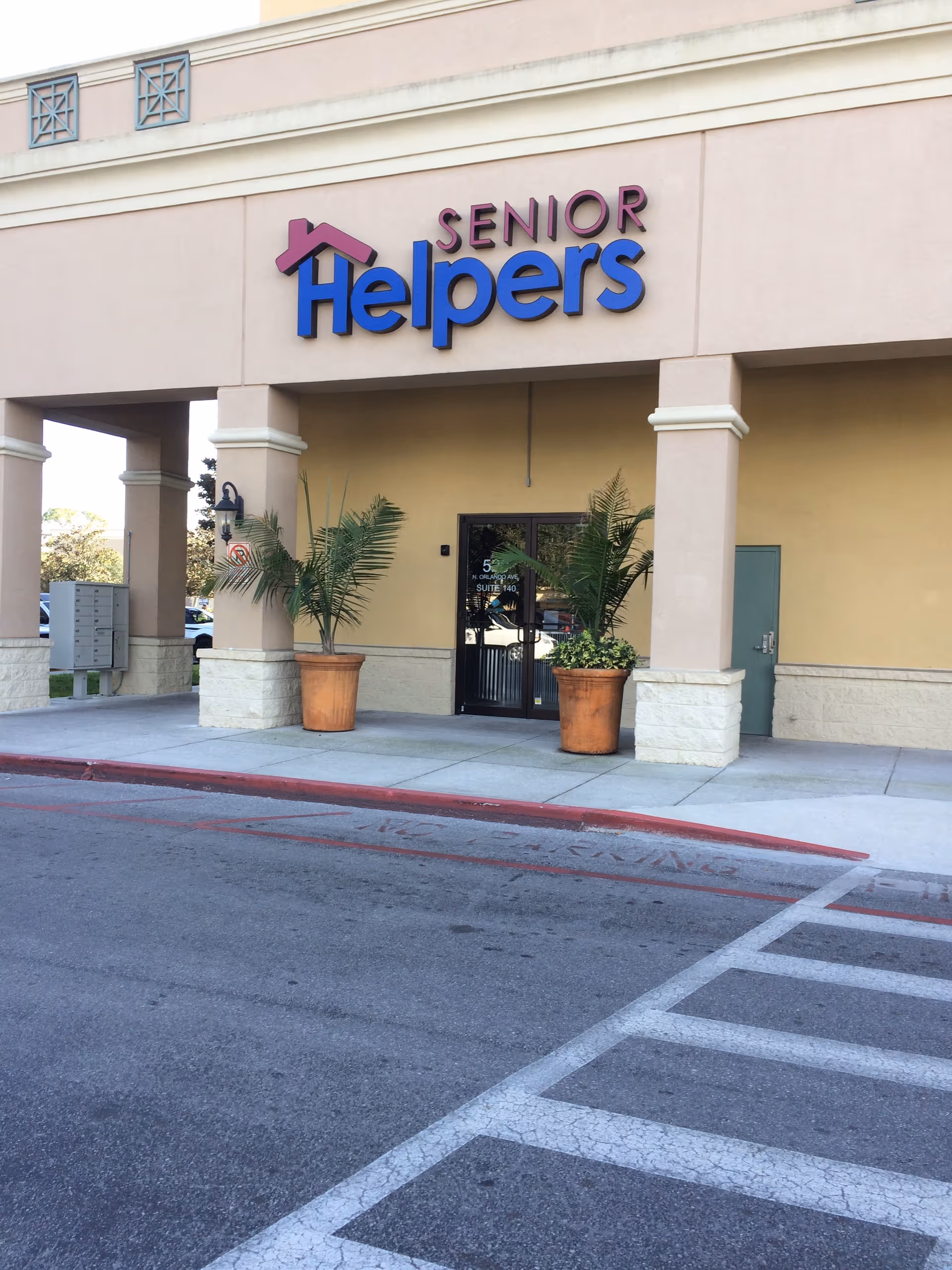 Exterior view of a Senior Helpers facility entrance with columns and potted plants.