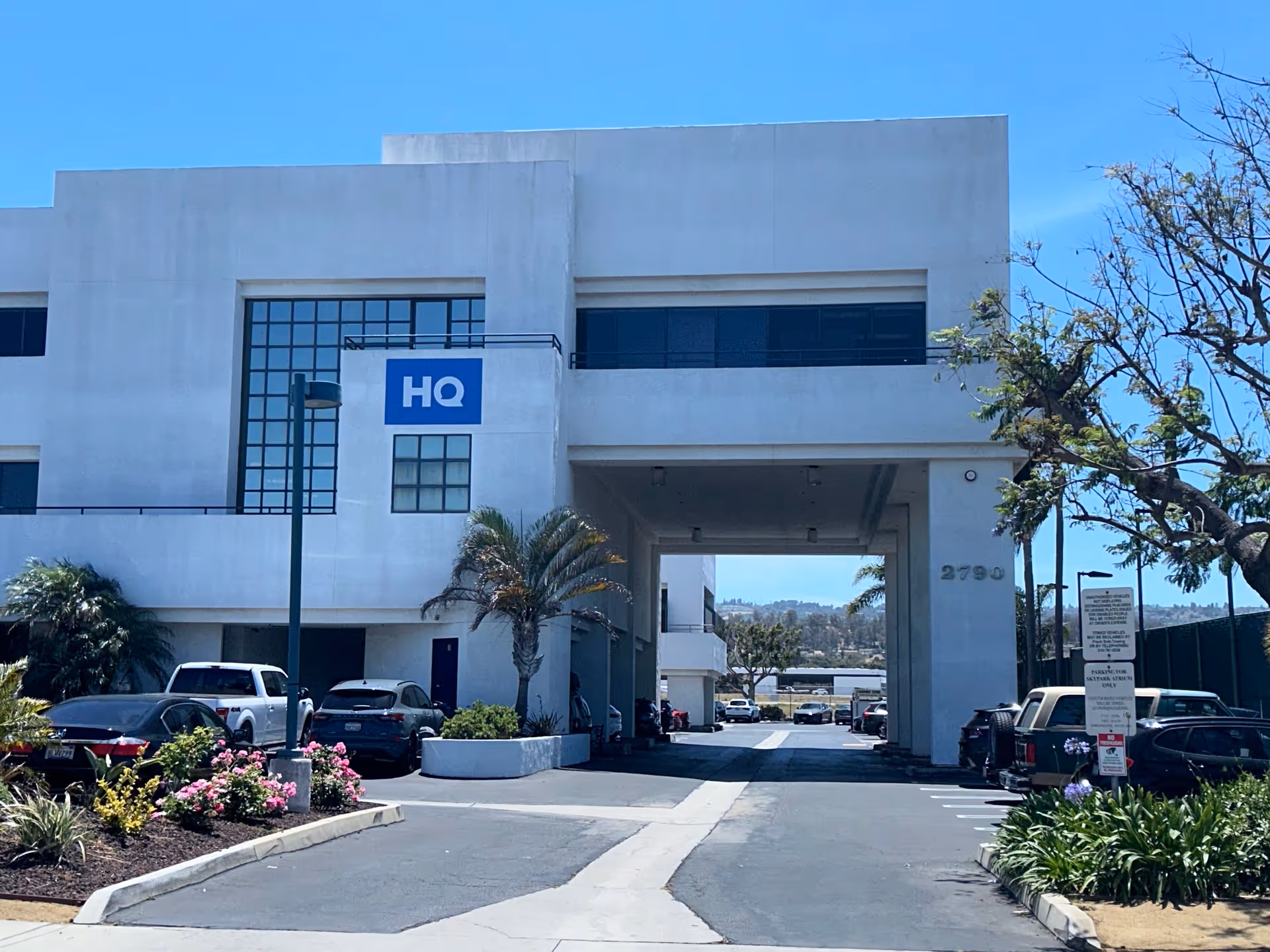 White modern building with an archway entrance, HQ sign, and parked cars.