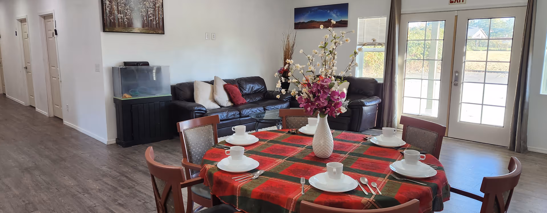 A dining table with a red plaid tablecloth and place settings in a communal living area.