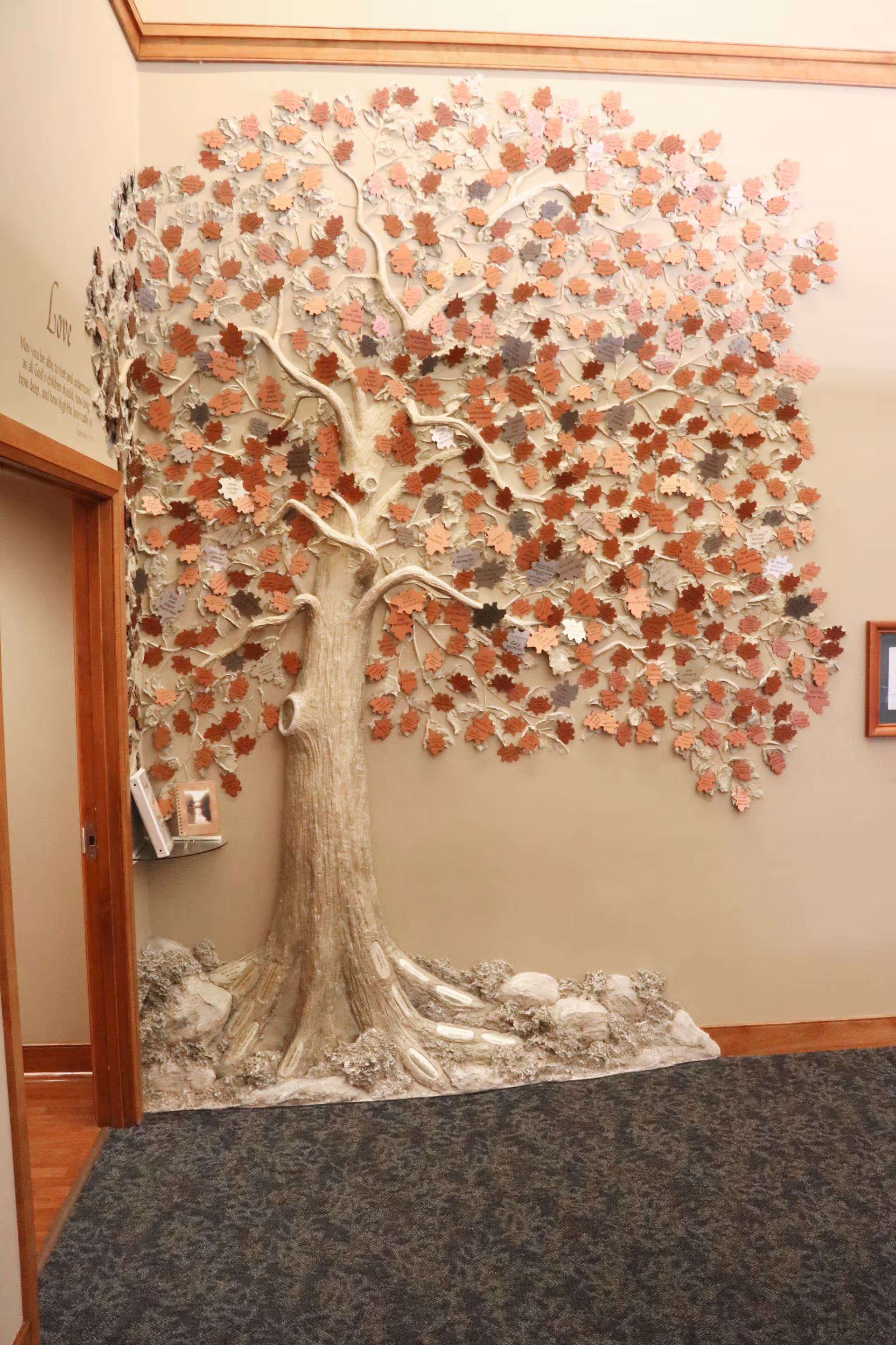 Large decorative tree sculpture with multicolored leaves on hallway wall inside a facility.