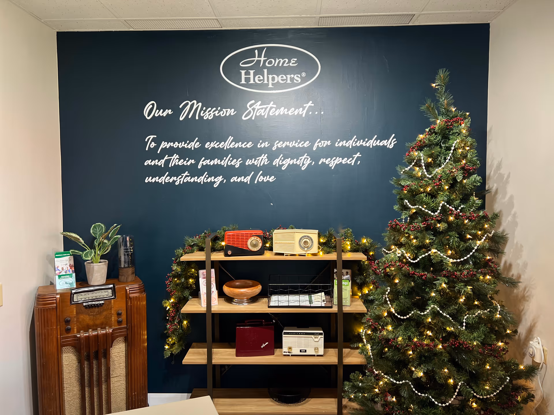 Interior room featuring a mission statement wall, shelf with retro radios, plants, and a Christmas tree.