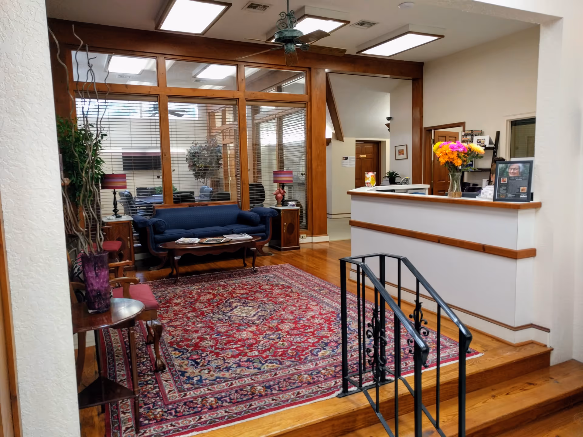 Senior living facility lobby with glass partitions, blue sofa, patterned rug, and front desk.