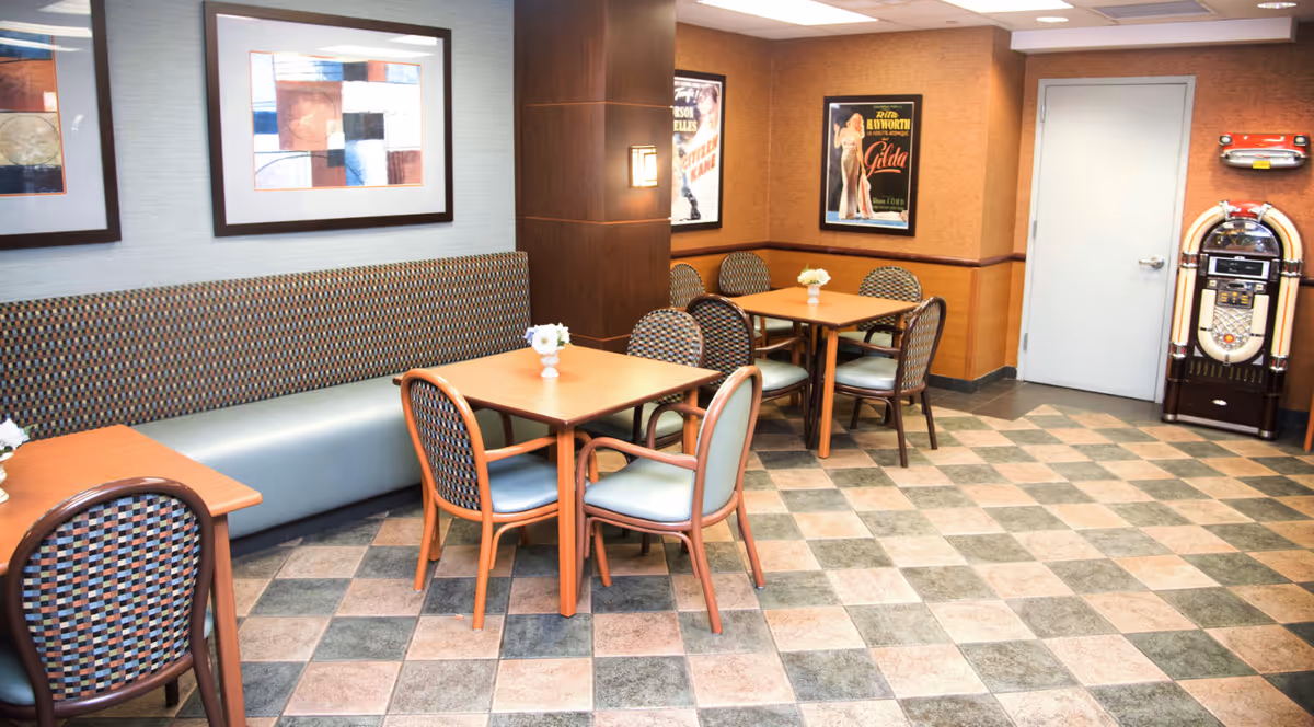 Inside senior living facility dining area with tables, chairs, bench seating, and a jukebox.
