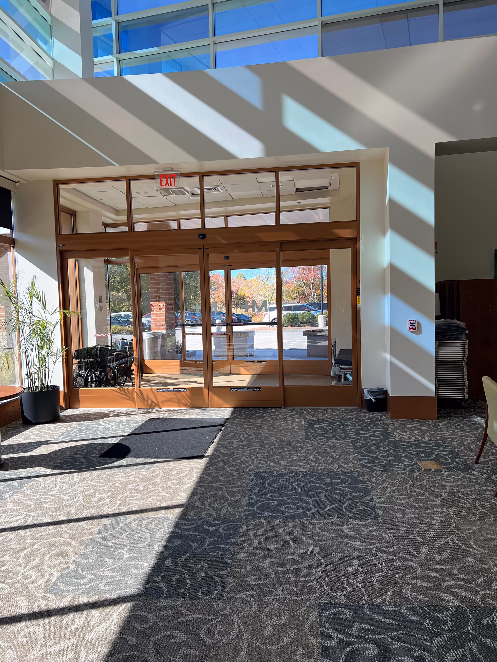 Interior lobby with glass doors, patterned carpet, a potted plant, and an exit sign.