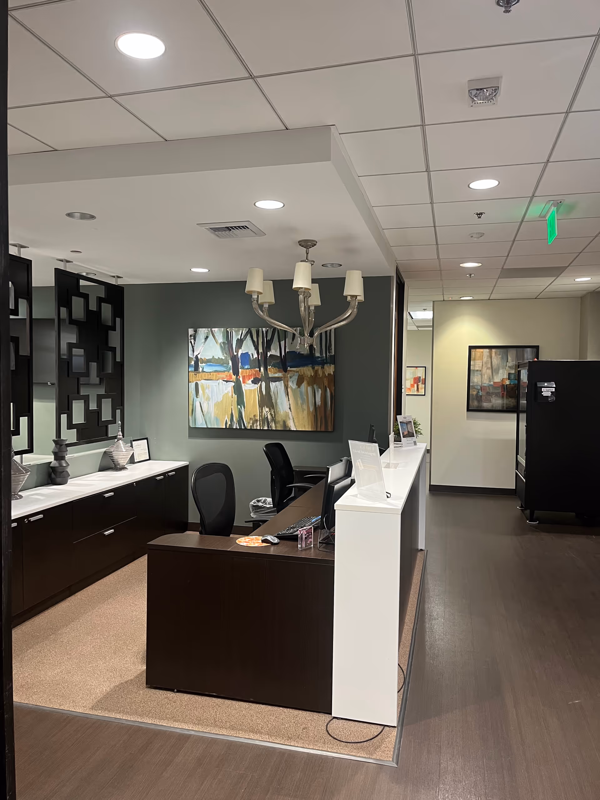 Reception area at Amada Senior Care featuring dark wood desk, seating, chandelier, and artwork.