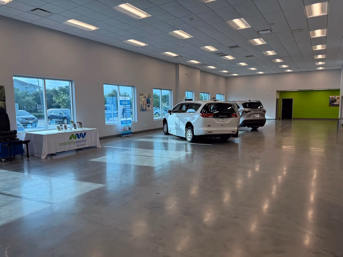 A spacious showroom with white cars inside, bright ceiling lights, and a MobilityWorks table.