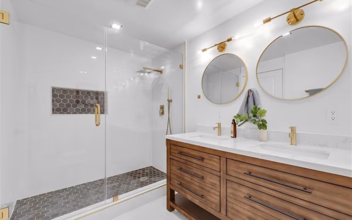 Modern white bathroom with glass shower, double sinks, and wooden vanity.