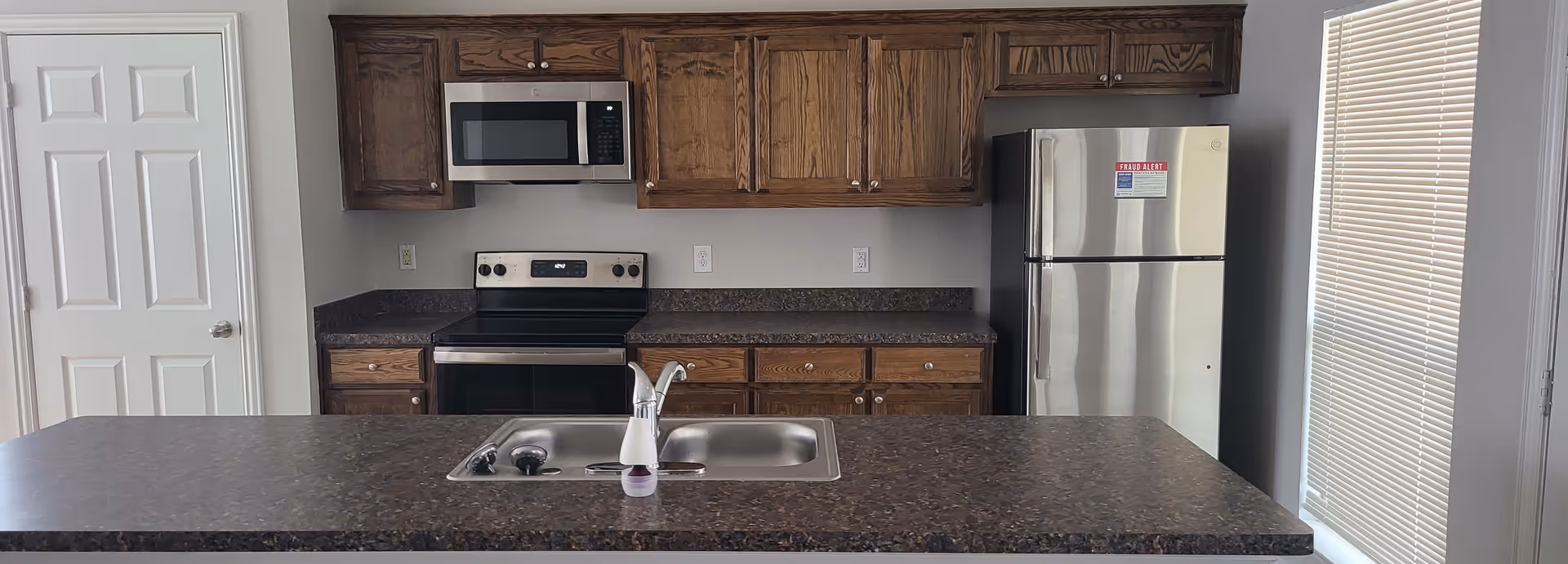 A modern kitchen with dark granite countertops, wooden cabinets, stainless steel appliances, and a sink island.