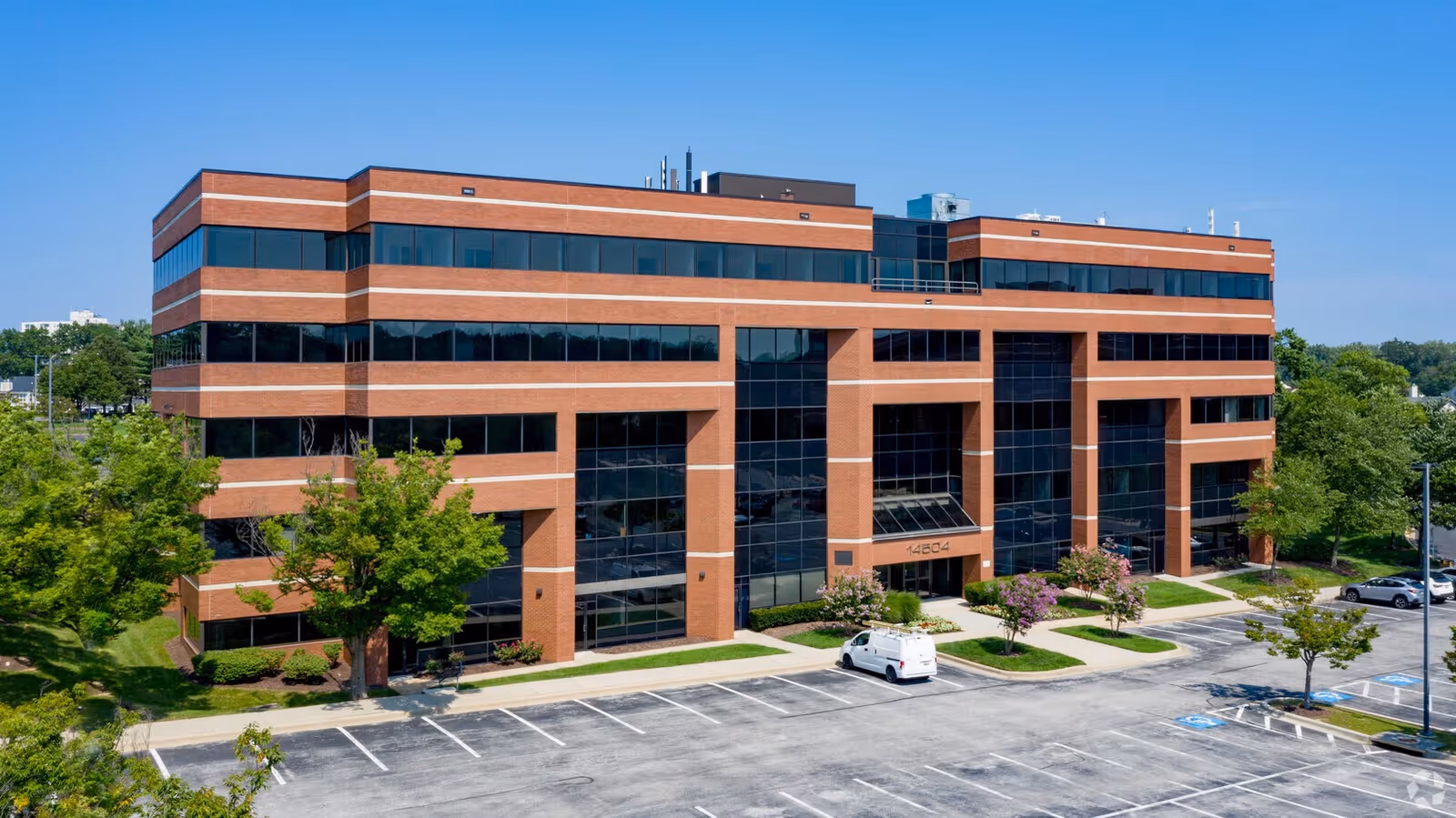 A brick multi-story building with large glass windows and a parking lot, viewed from above.