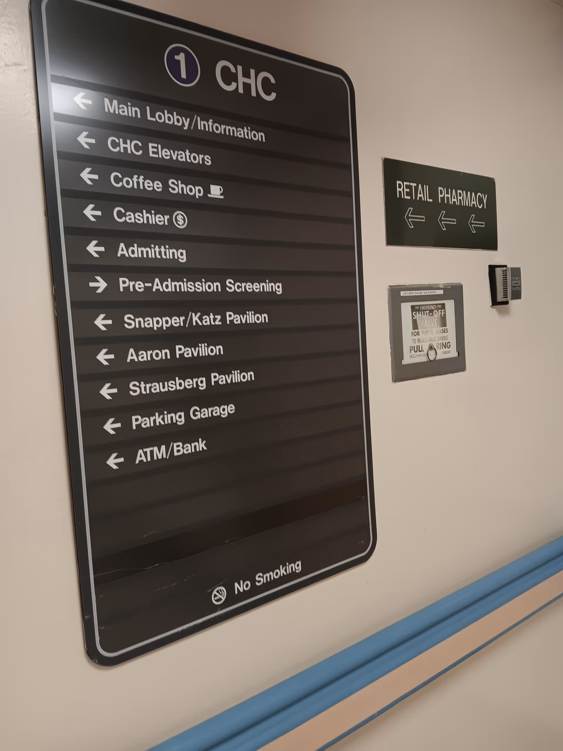 Large black hallway signboard with arrows listing hospital services in a medical center.