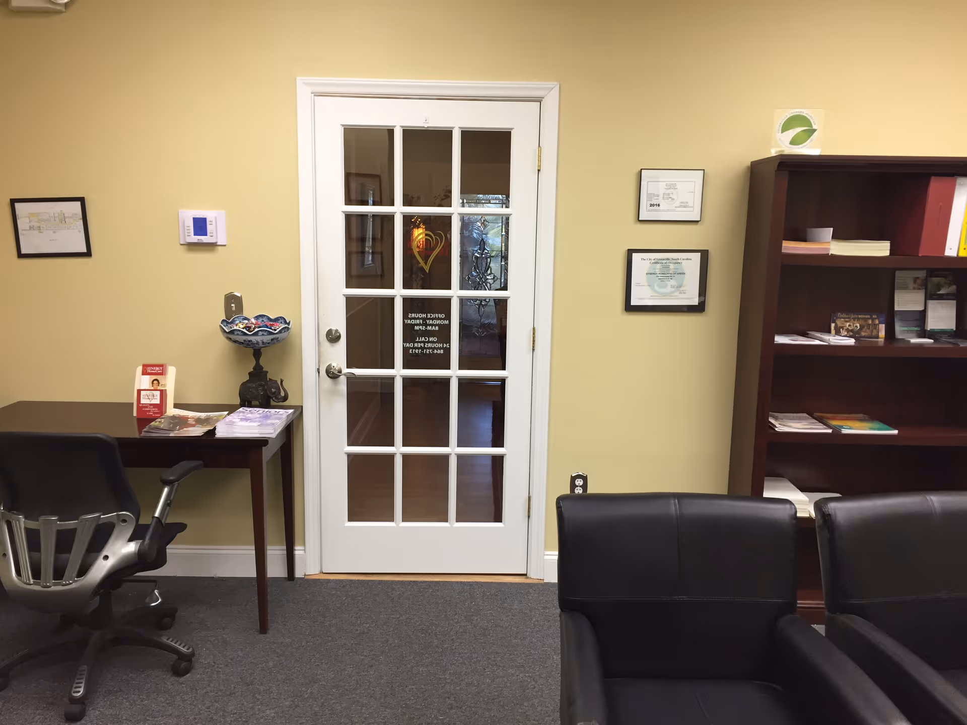 Reception area with a glass-pane door, desk, bookshelf, and black leather chairs.