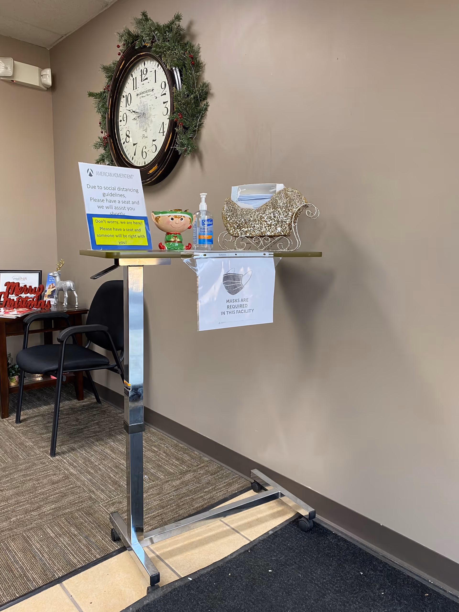 Interior reception area with a large clock, holiday decor, and safety signage on a standing table.