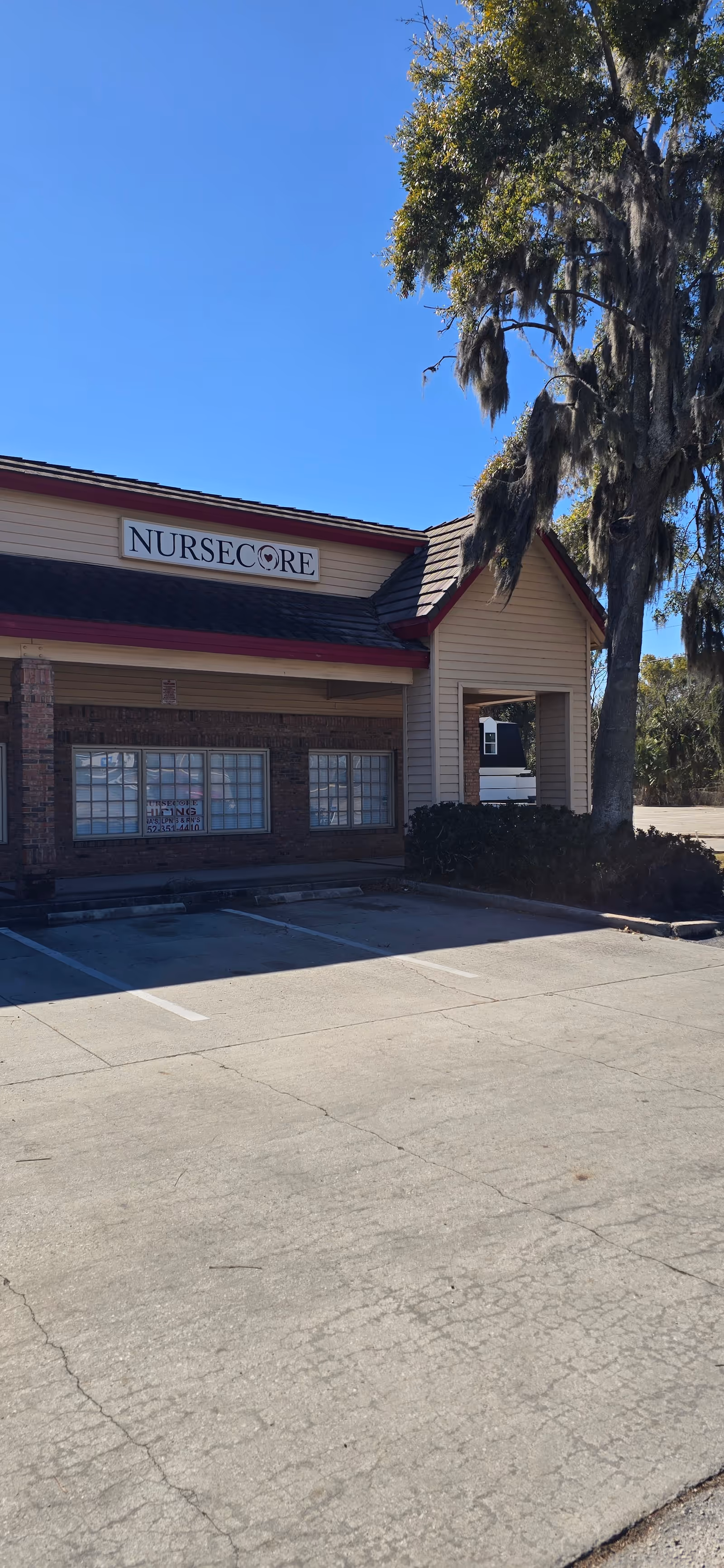 Exterior view of a NurseCore building front with sign, parking lot, and a large tree.