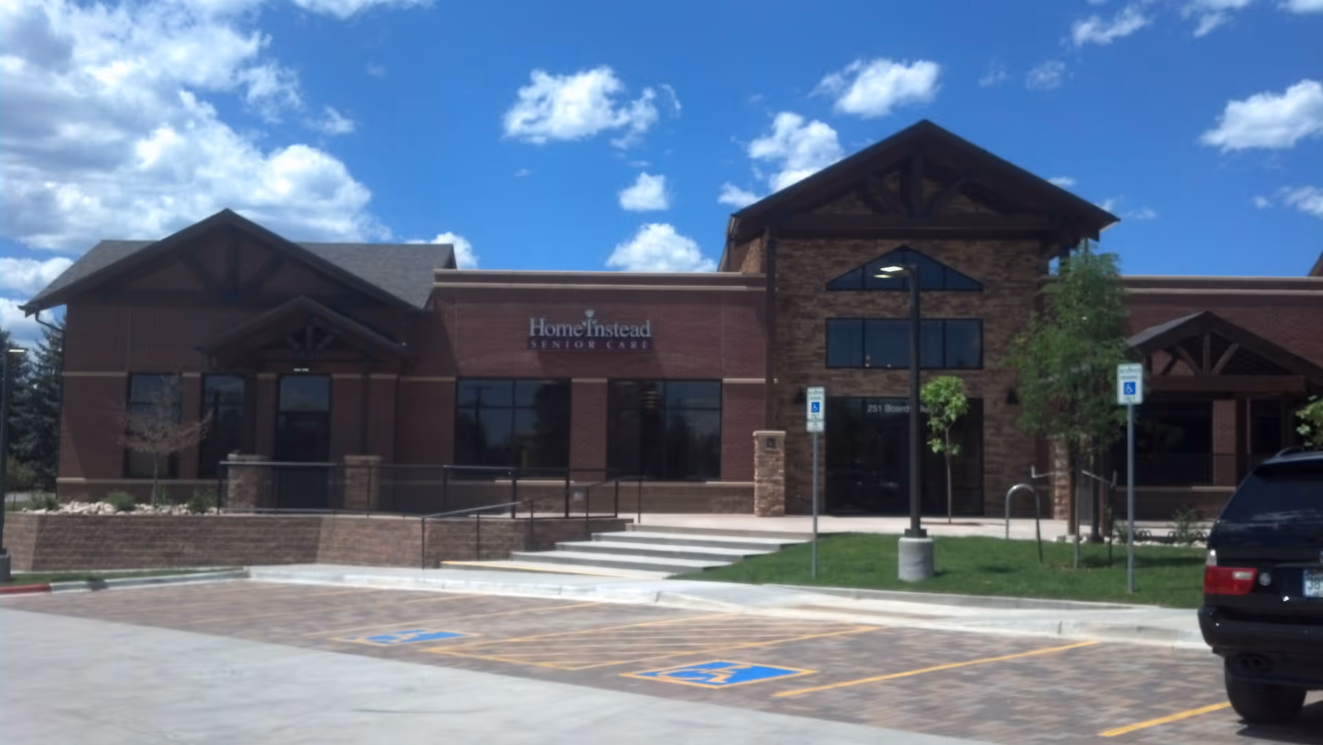 Brick building with Home Instead sign, glass doors, and a parking lot in front.