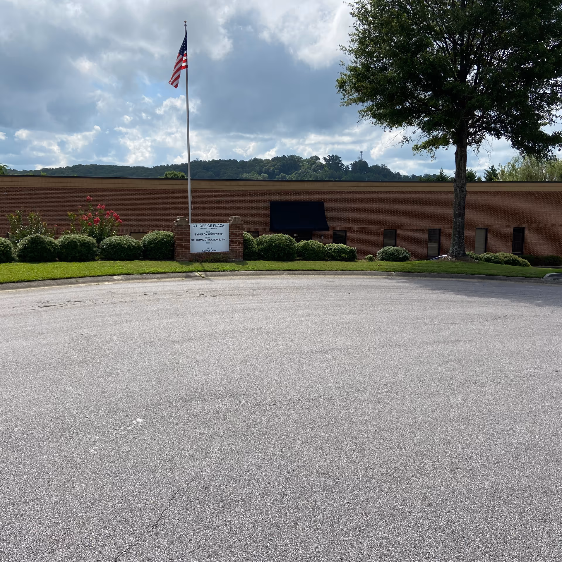Exterior view of a brick senior care building with a flagpole, sign, and landscaped shrubs.