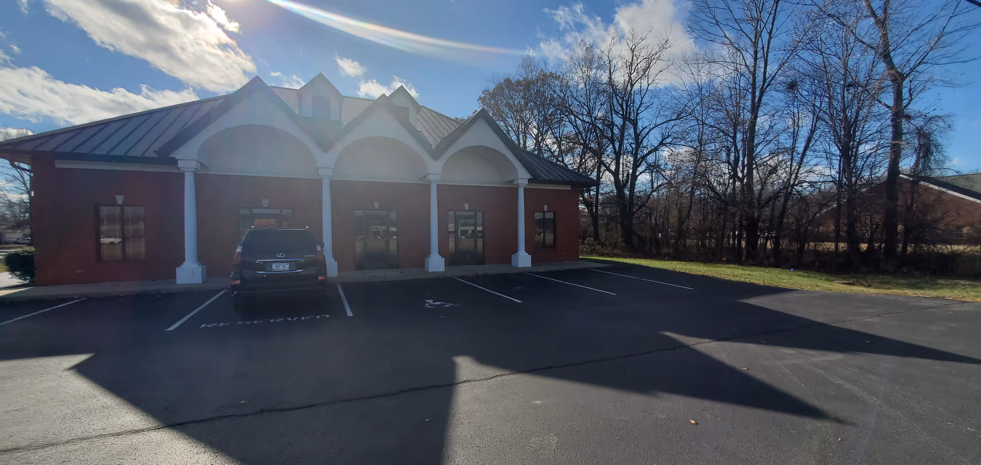 Brick facility with arched entrance and white columns, parked car visible.