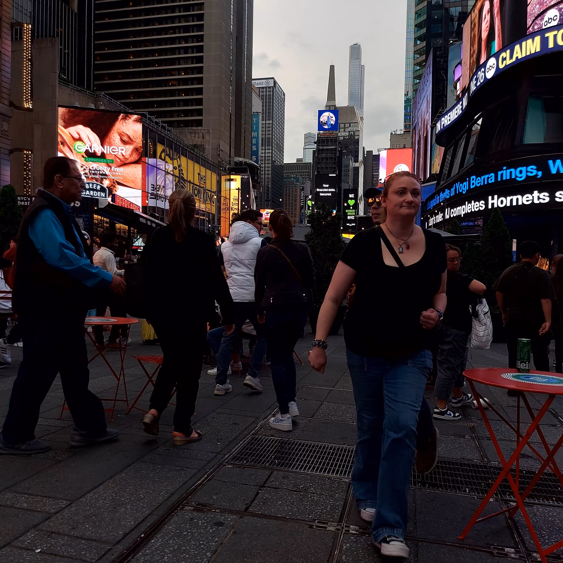 Crowded city square with pedestrians and bright digital billboards at dusk.