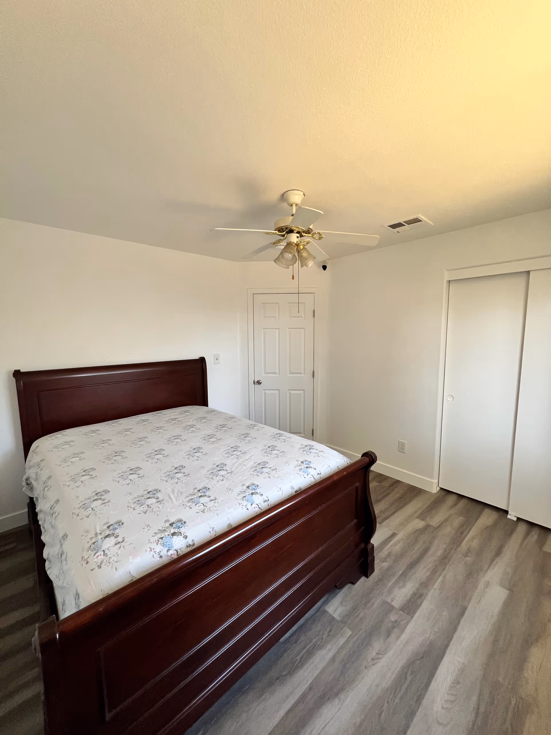 Bedroom with a dark wood bed, gray wood-look flooring, ceiling fan, and closet.