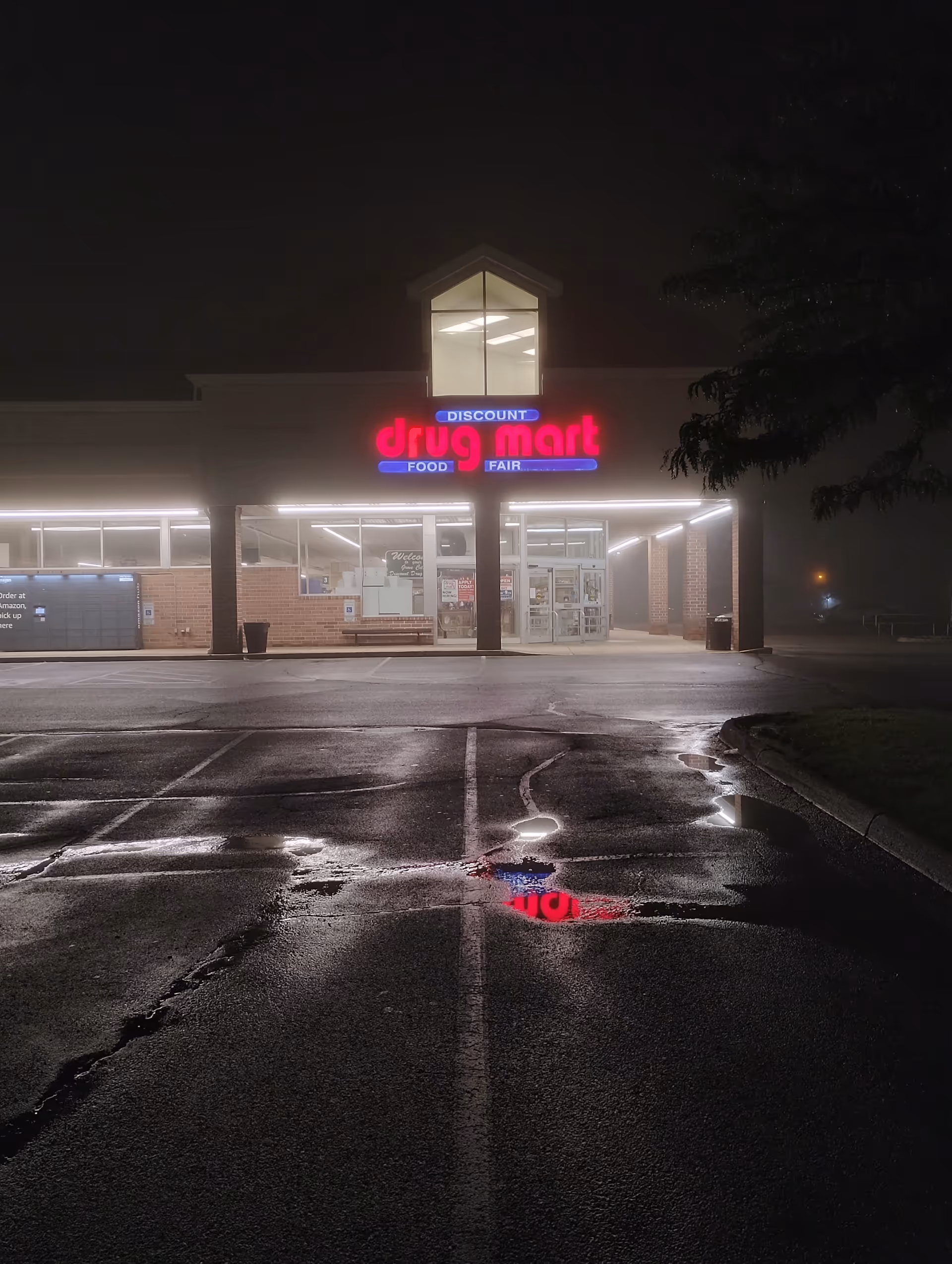 Nighttime view of Discount Drug Mart storefront with neon sign and wet parking lot.