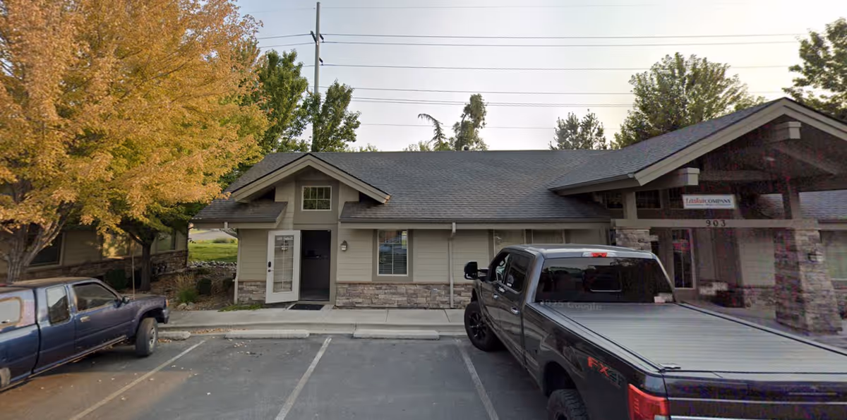 Front view of a single-story Senior Helpers building with parked trucks and trees.