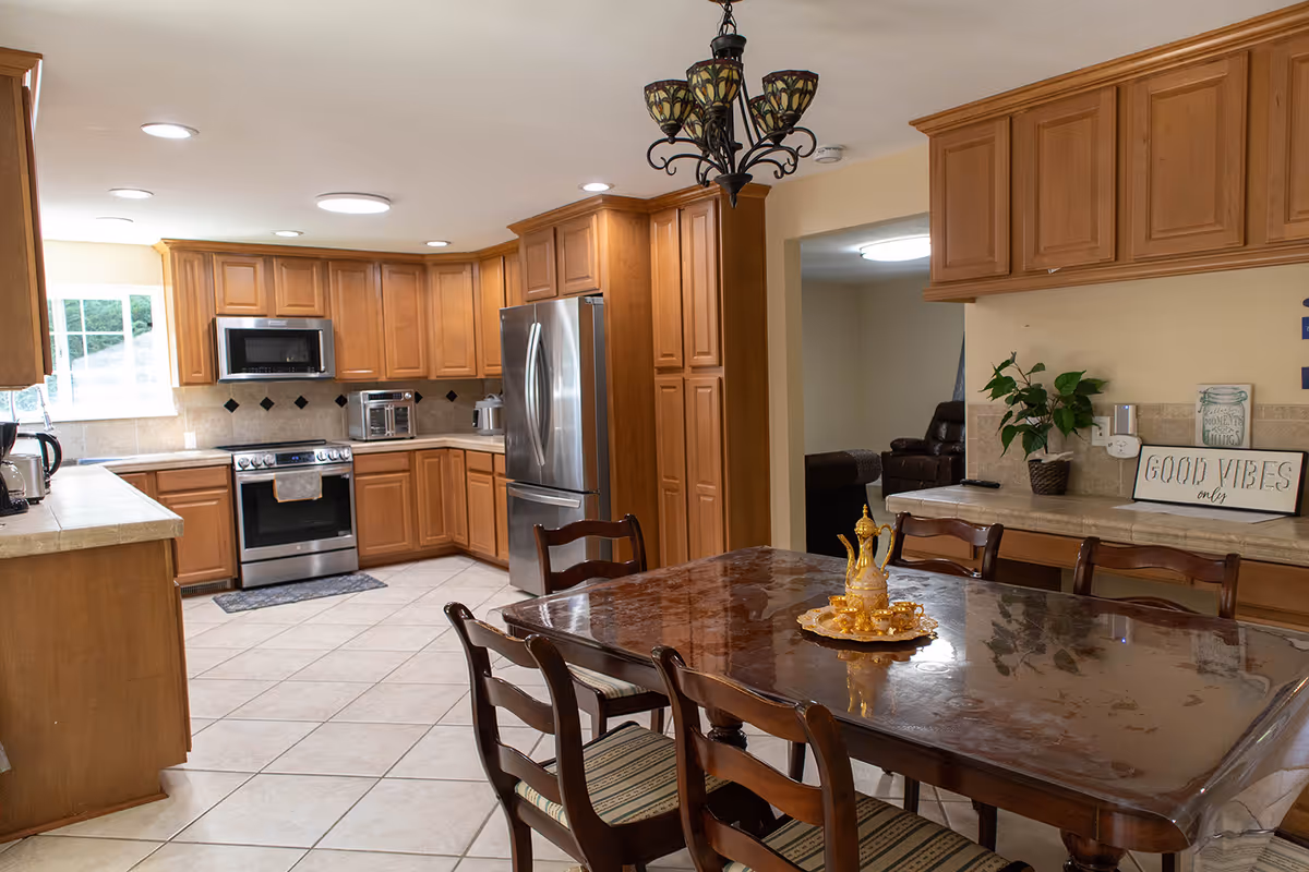 Open kitchen and dining area with wooden cabinets, stainless appliances, and a polished table.