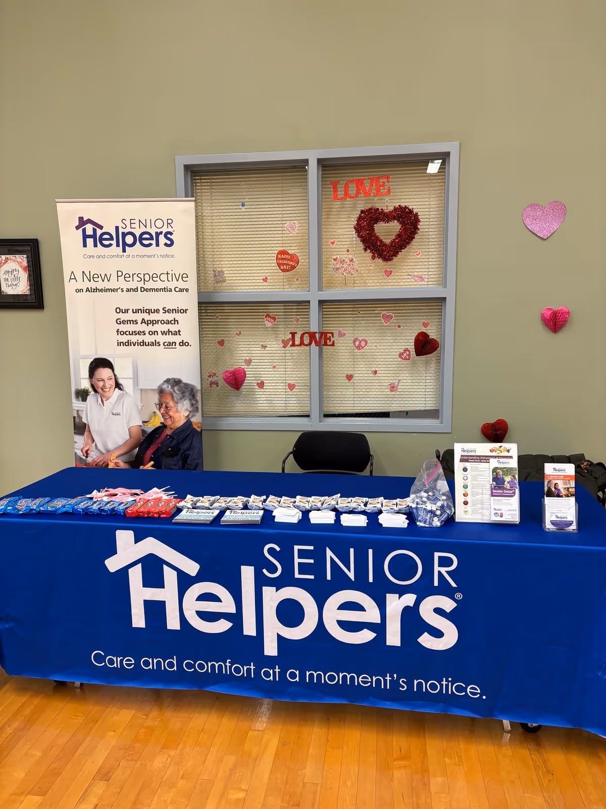 Senior Helpers information table inside a decorated interior with heart-themed window art.