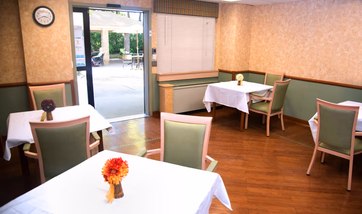 Dining room with white-cloth tables, green chairs, and floral centerpieces; door to outside patio.