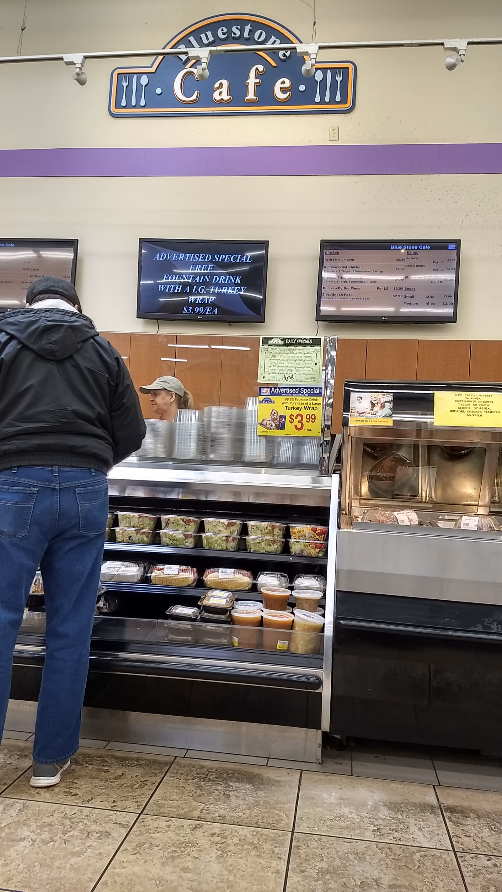 Shoppers stand at a cafe counter with displays and menu boards inside a store.