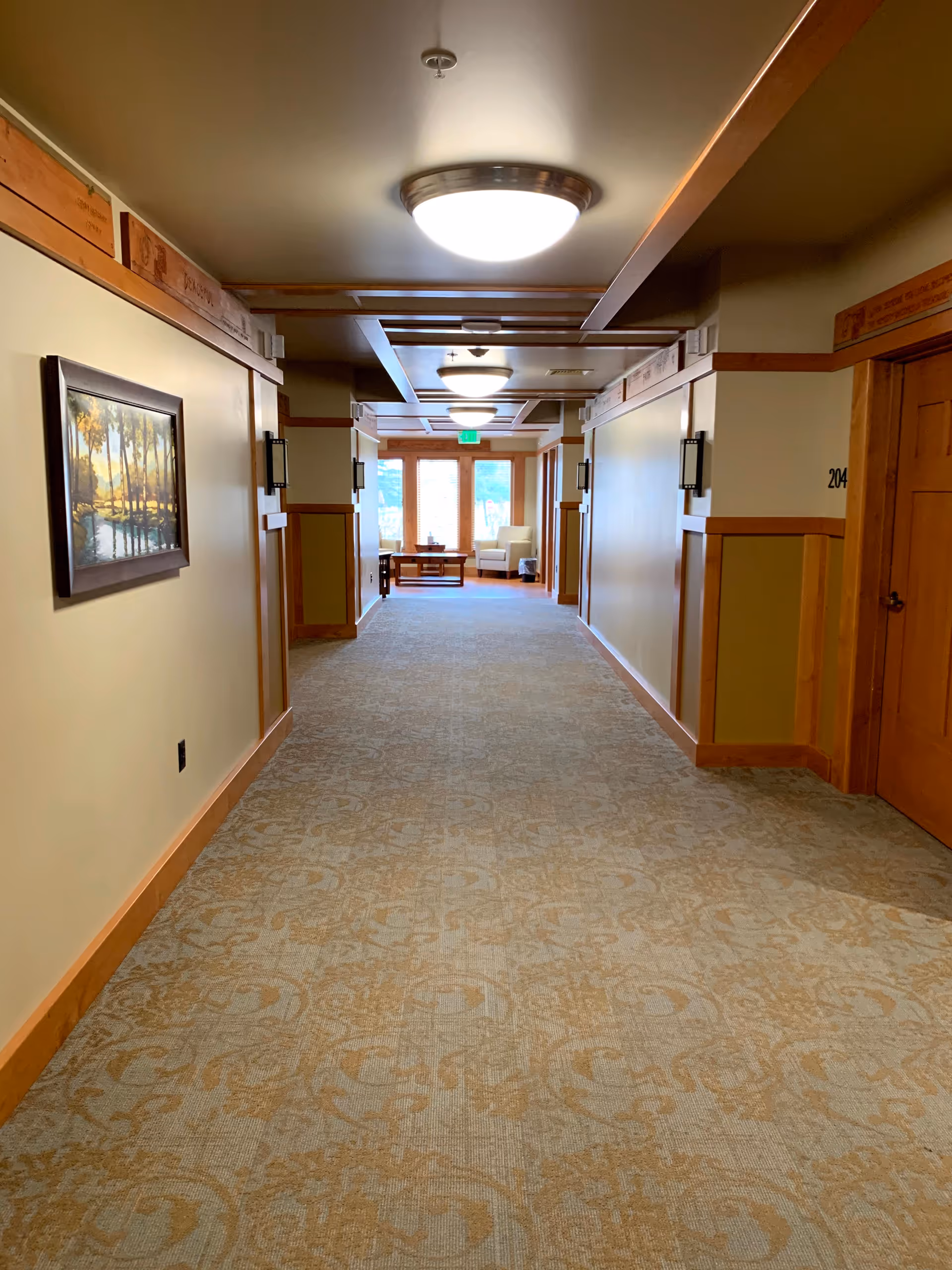 Long carpeted hallway in a senior living facility with seating at the end.
