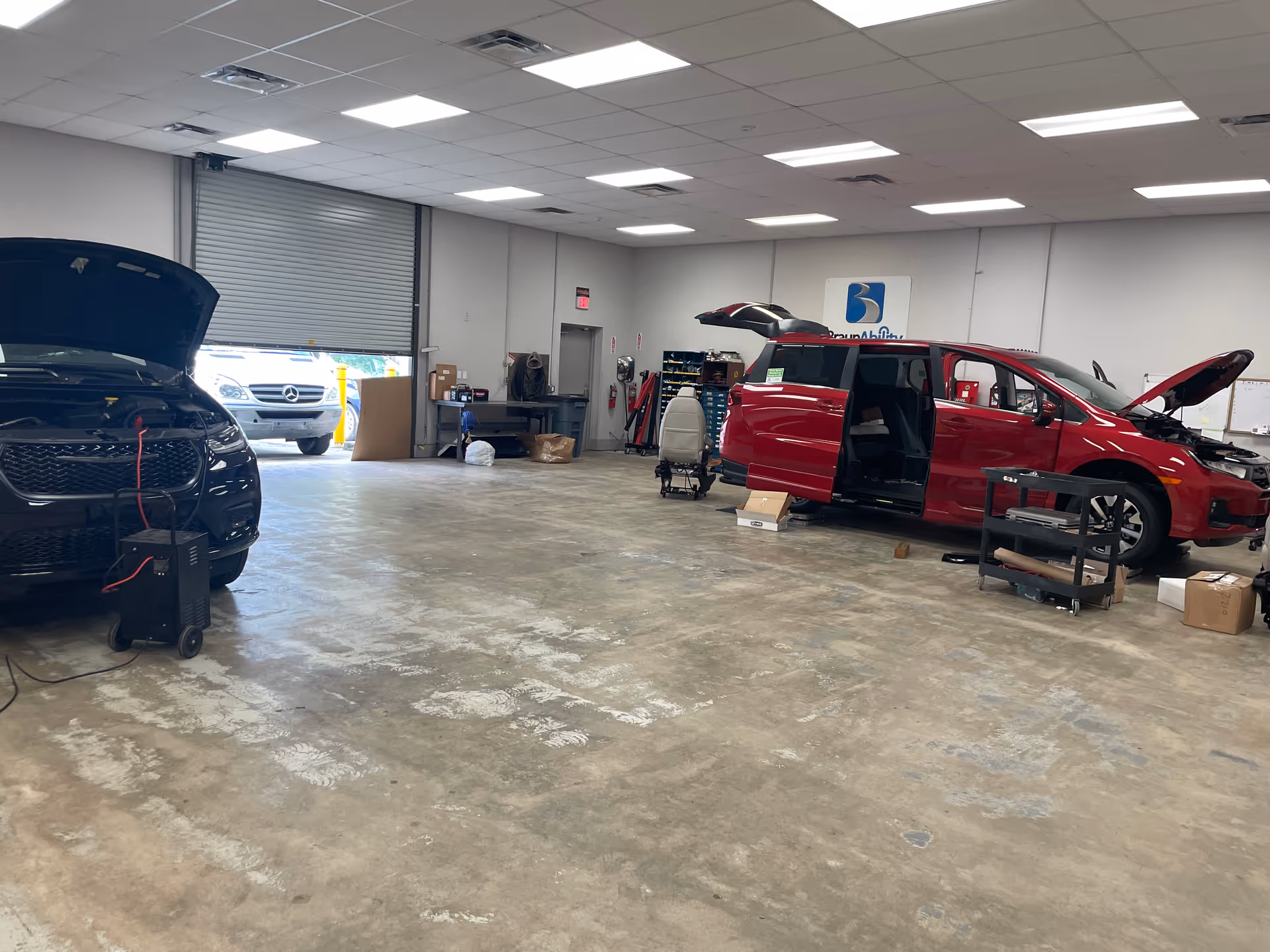 Inside a large service garage with two cars and workshop equipment.