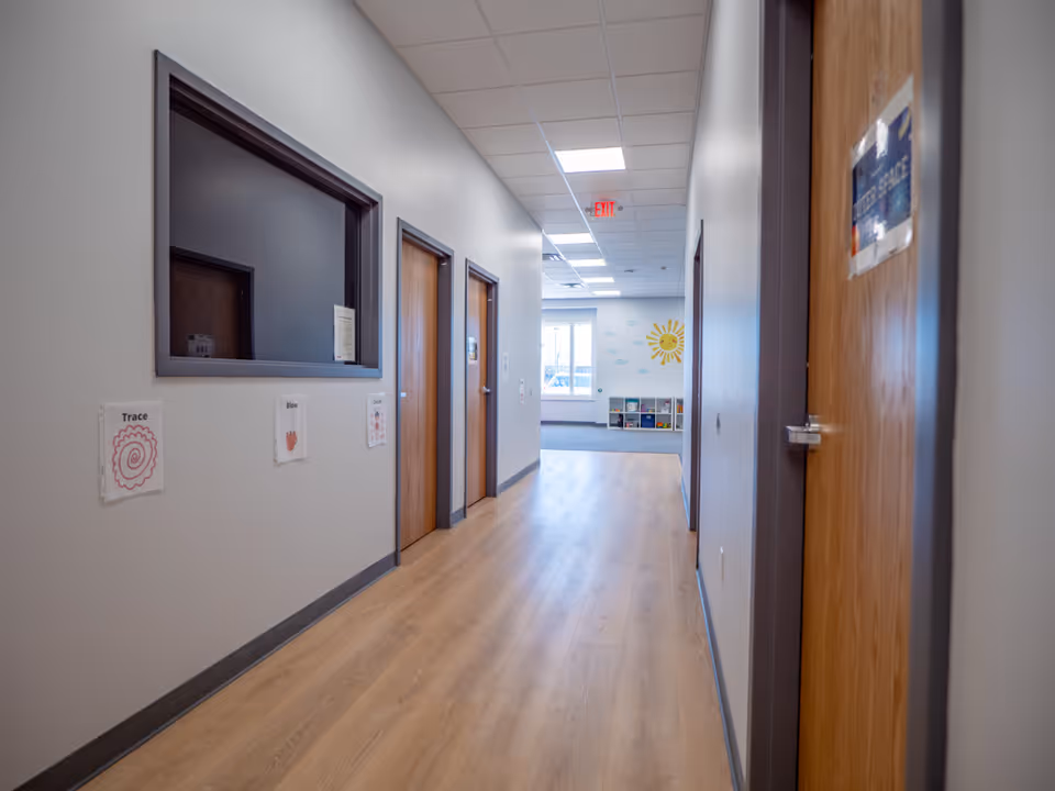 Interior hallway of a facility with doors, artwork, and sunlit end room.
