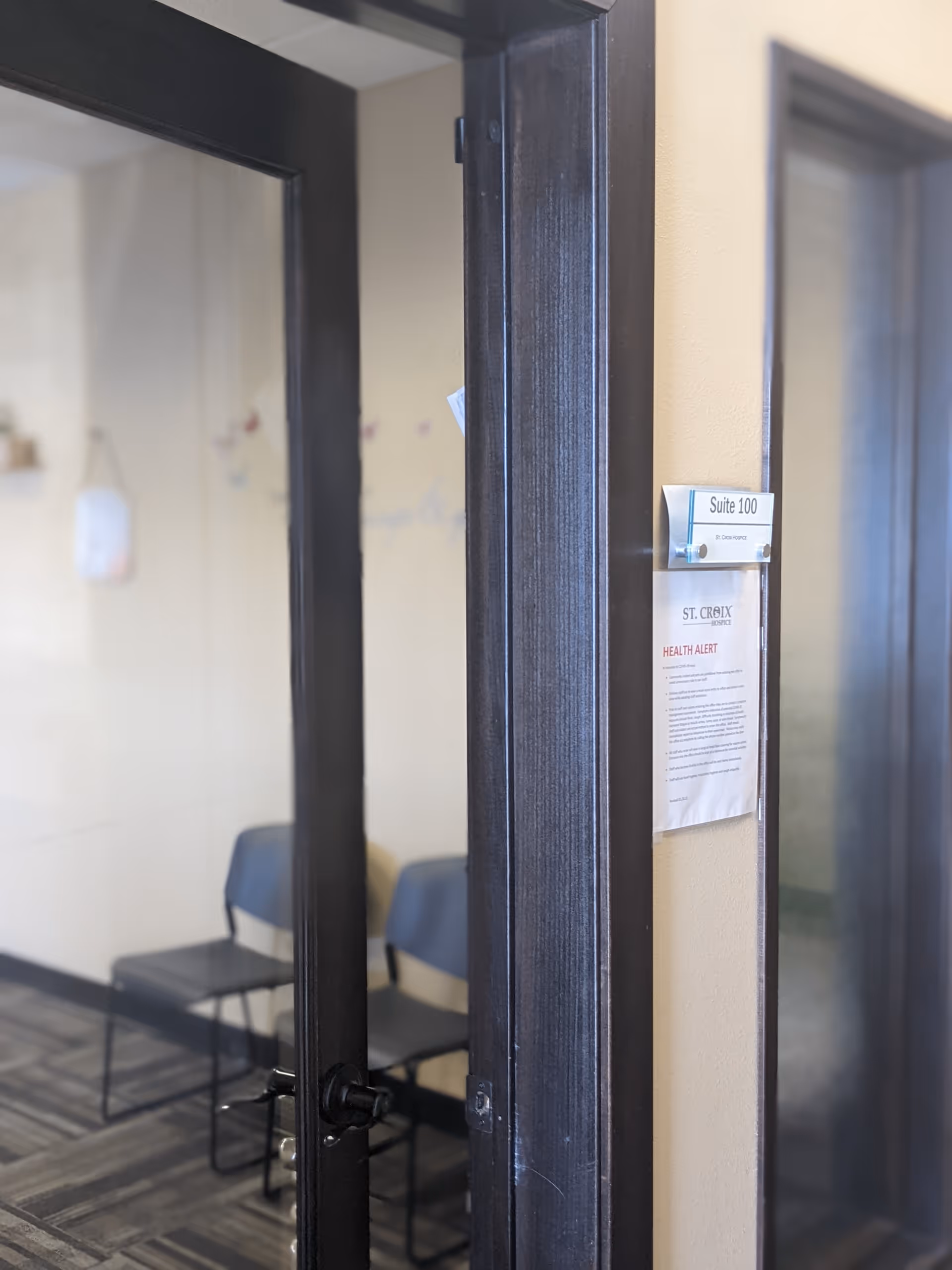 Open glass doors reveal a waiting area with two blue chairs.