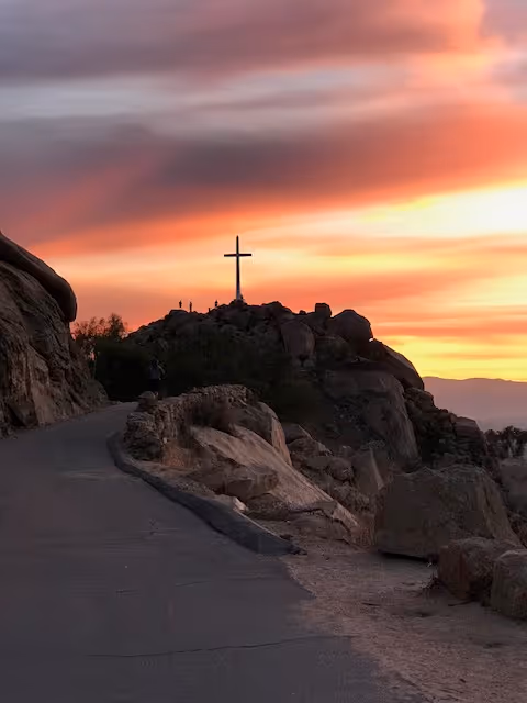 Sunset over rocky hill with a cross at the summit and winding path