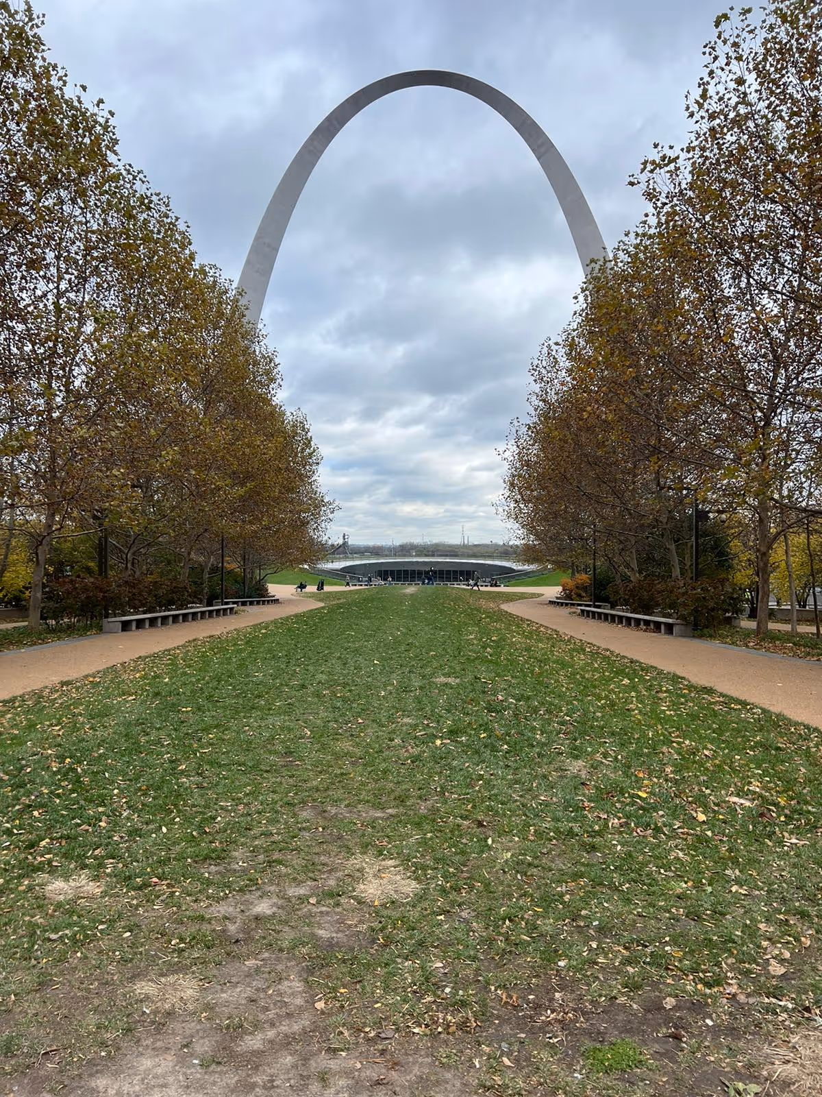 Wide park path with benches and trees, leading toward the Gateway Arch in the distance.