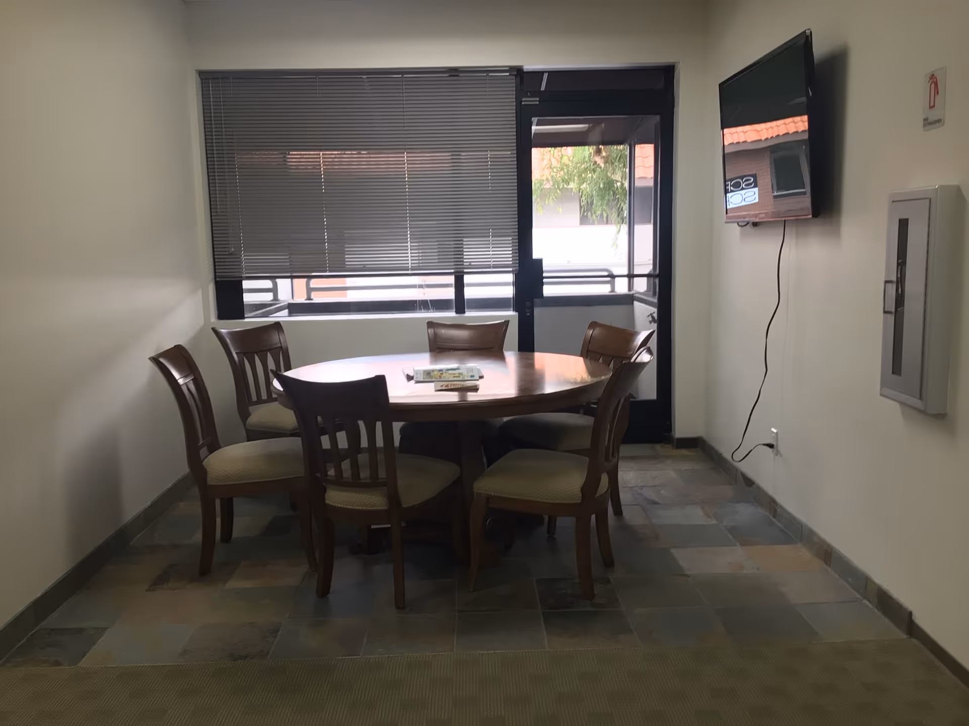 Round wooden dining table with six chairs in a small indoor dining area.