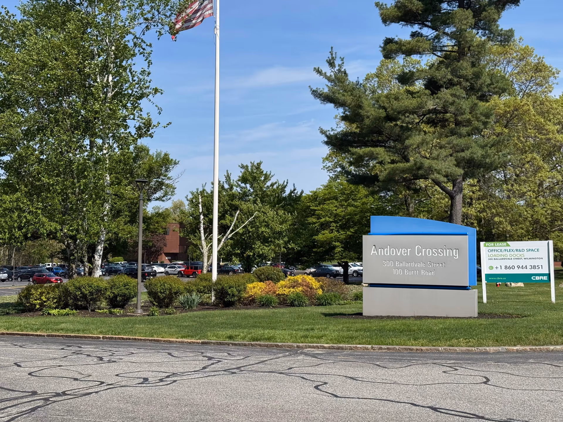 Outdoor view of Andover Crossing entrance with flagpole, sign, landscaping, and parked cars.