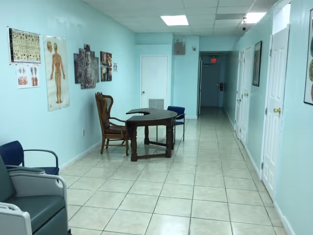 Long turquoise hallway in a senior facility with chairs, a round table, and medical posters.