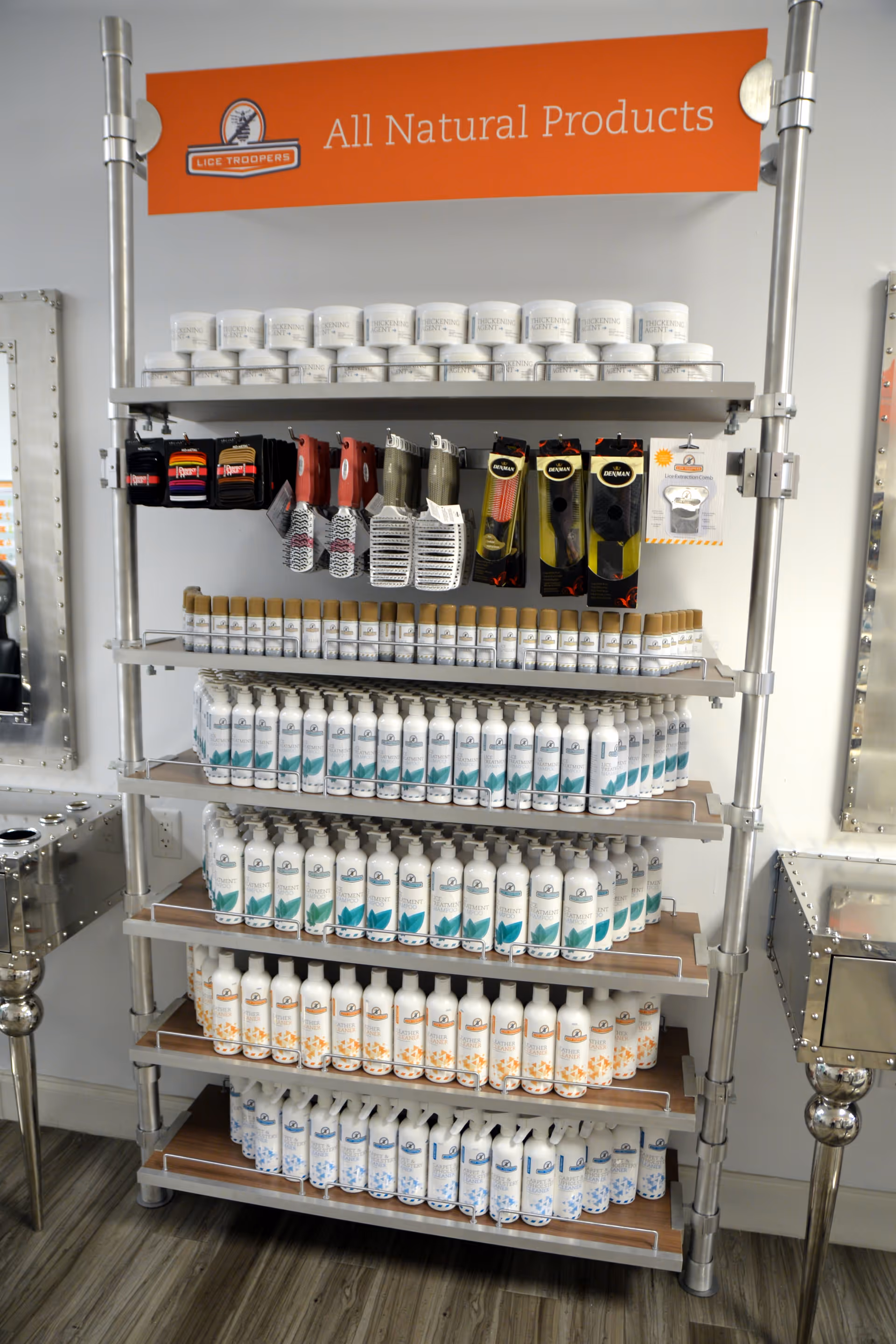 Orange banner says All Natural Products above a metal shelf stocked with lice treatment products.