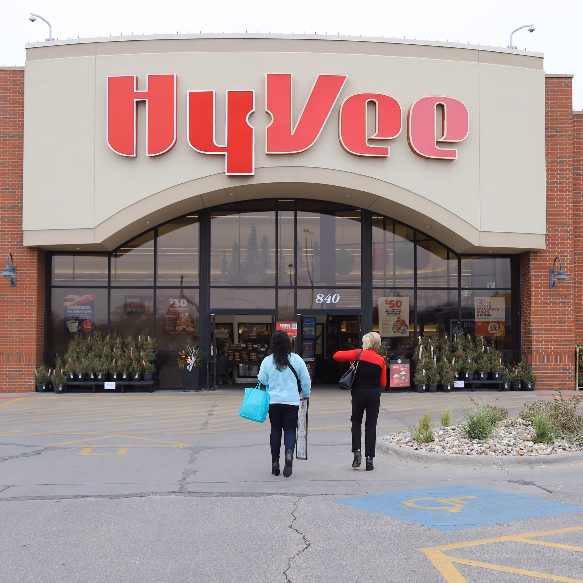 Two shoppers approach the Hy-Vee storefront entrance outside.