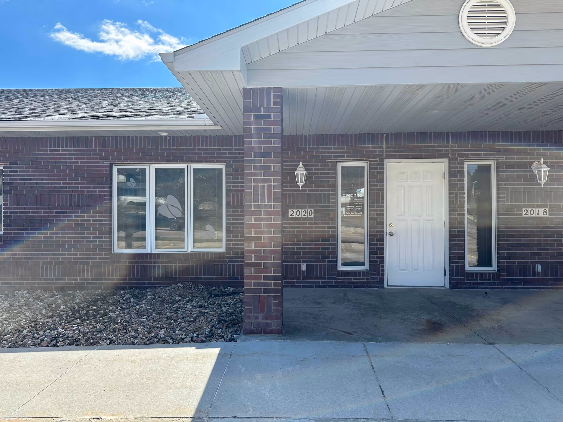 Brick facility entrance with white door and windows under a covered front porch.