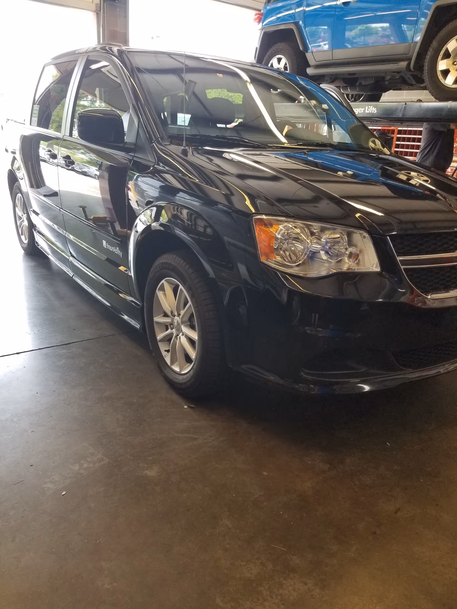 Black sedan inside a service bay with a blue SUV raised on a lift.